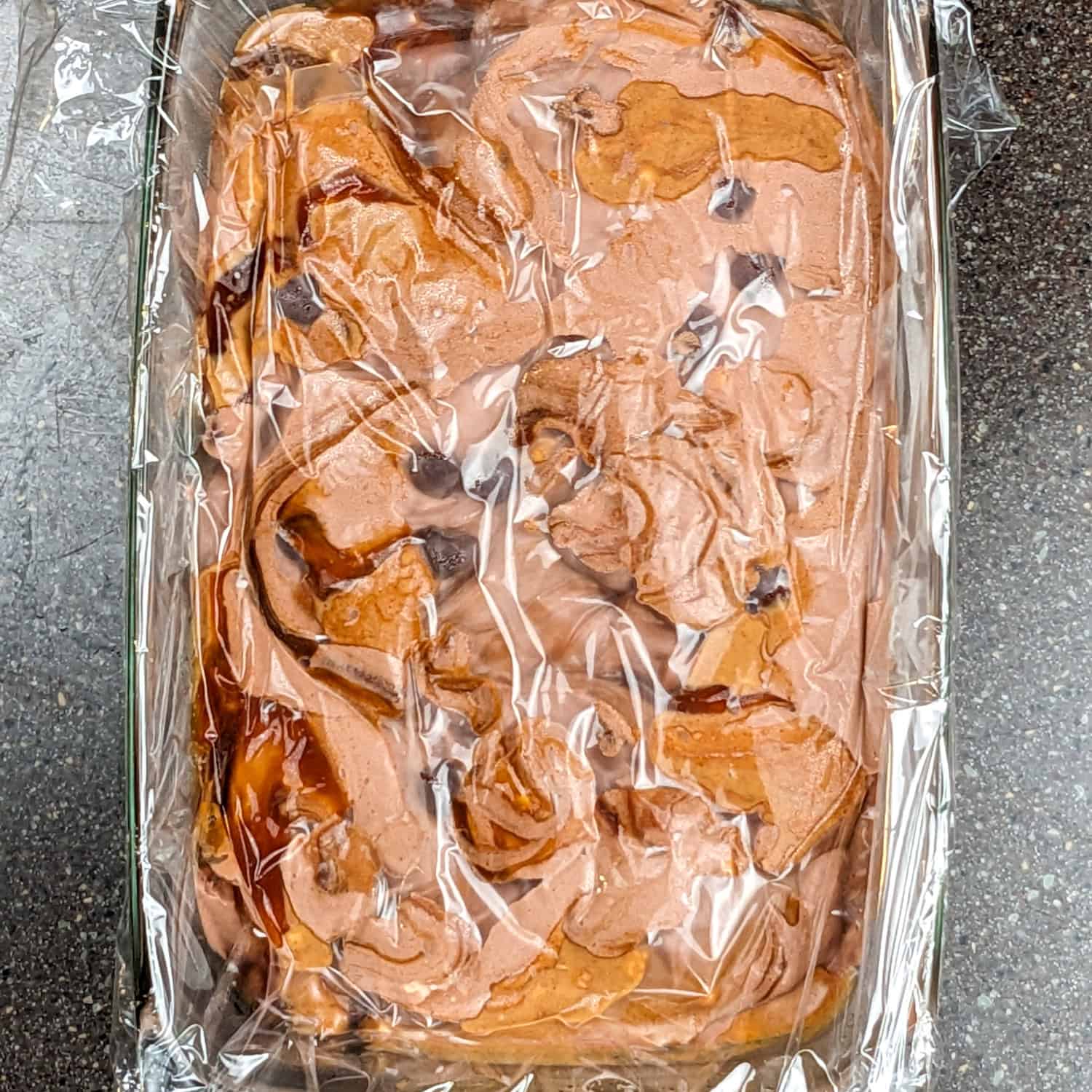 Rich chocolate ice cream base in a glass baking dish, covered with plastic wrap for the freezer.